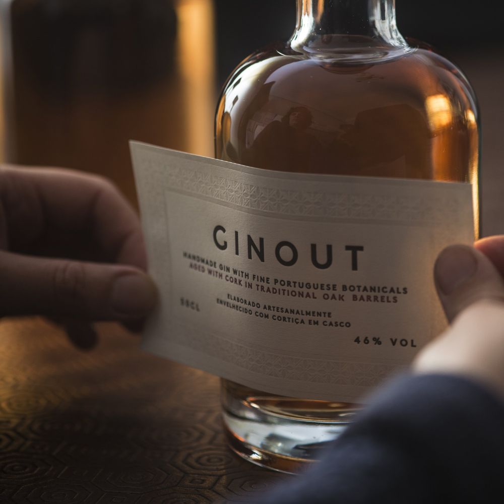 Quel gin choisir ? Étiquette artisanale apposée sur une bouteille de gin portugais GINOUT, élaboré avec des botaniques locales et vieilli en fût de chêne. Le Club des Connaisseurs