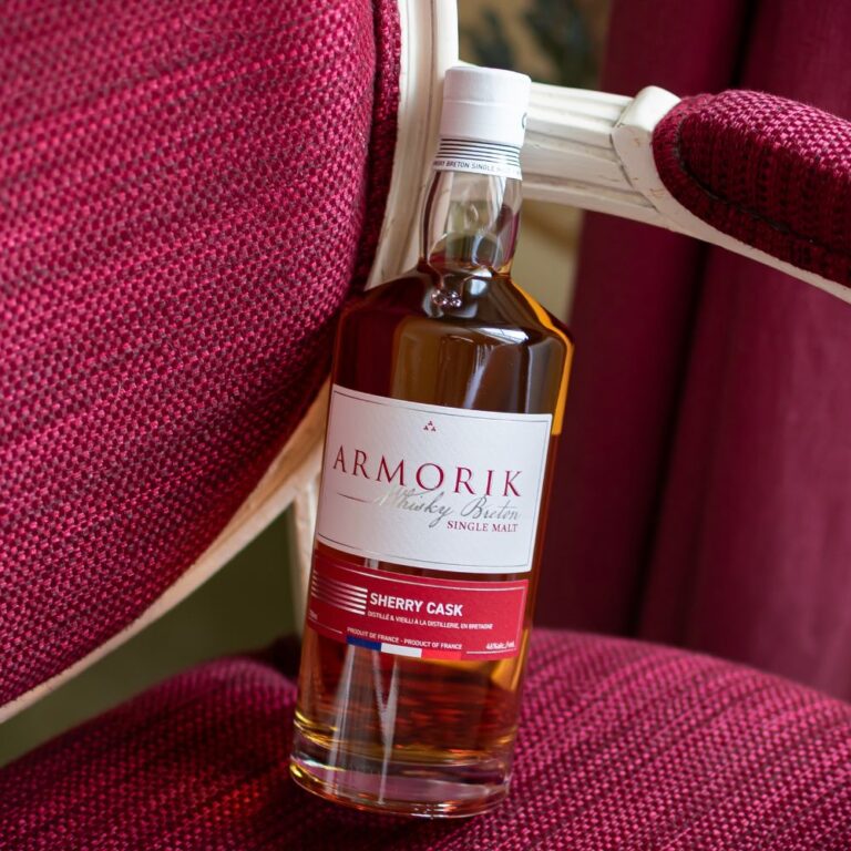 Whisky Armorik Sherry Cask mis en scène sur un fauteuil en tissu rouge, single malt breton vieilli en fût de sherry, whisky français premium. Le Club des Connaisseurs
