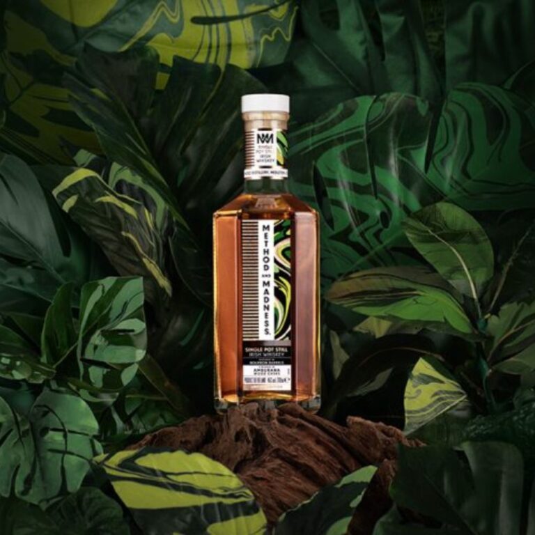 Bouteille de whisky Method & Madness Single Pot Still placée sur une souche d’arbre, entourée d’un décor luxuriant de feuilles vertes avec des motifs artistiques en arrière-plan. Le Club des Connaisseurs.