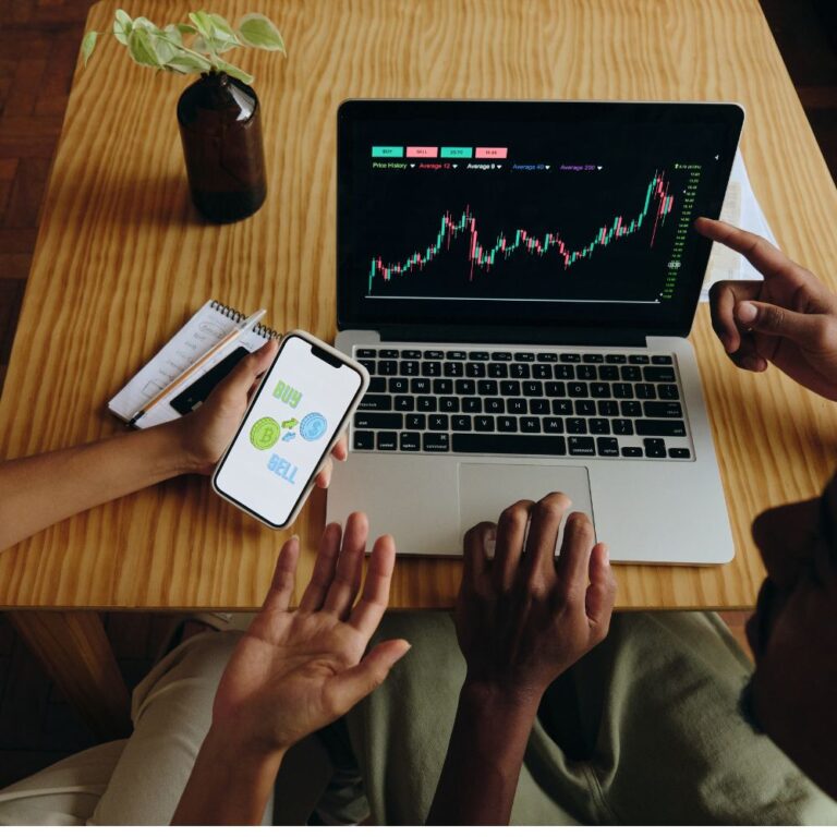 Miniature de l'article de blog Investir dans le whisky. Personnes utilisant un ordinateur portable affichant un graphique de trading, et un téléphone avec les options buy et sell. Le Club des Connaisseurs.