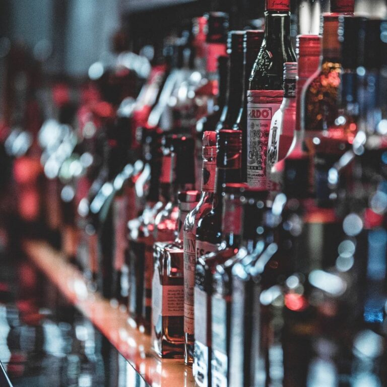 miniature article de blog rhum conservation, Alignement de nombreuses bouteilles de spiritueux sur un bar, avec des étiquettes colorées et une ambiance tamisée. Photo idéale pour illustrer l'univers du whisky et de l'investissement dans les spiritueux - Le Club des Connaisseurs.