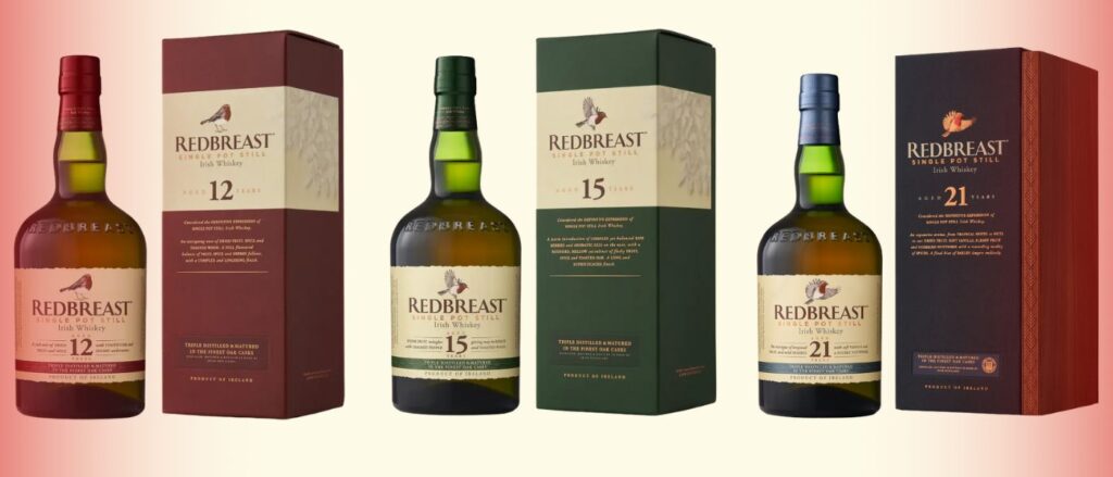 Les trois bouteilles phares de Redbreast whiskey irlandais : Redbreast Single Pot Still 12, 15 et 21 ans accompagnées de leurs coffrets respectifs, disposées sur un fond dégradé rouge clair. Le Club des Connaisseurs.