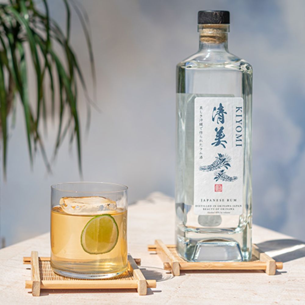 Beautyshot de la bouteille de rhum blanc japonais Kiyomi accompagnée d’un cocktail au citron vert sur fond lumineux.