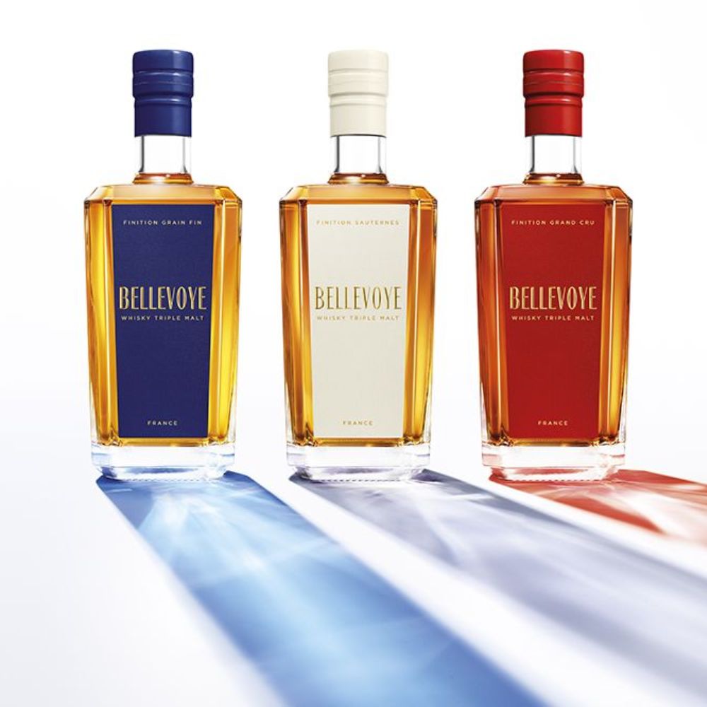 Beautyshot de trois bouteilles de whisky français Bellevoye aux finitions Grain Fin, Sauternes et Grand Cru, avec reflets tricolores bleu, blanc et rouge sur fond blanc.
