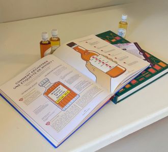 Livres de dégustation sur le whisky ouverts, expliquant comment lire une étiquette de bouteille, accompagnés de fioles de whisky pour une initiation à la dégustation.