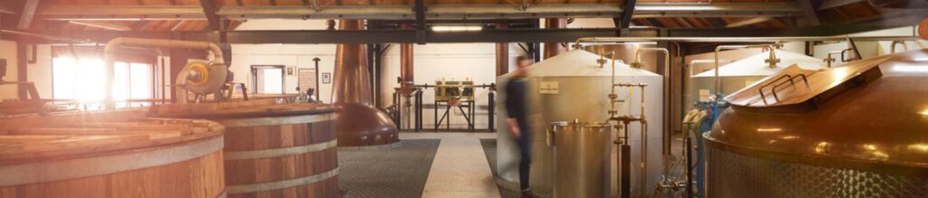 Cuves de fermentation et alambics en cuivre dans une distillerie traditionnelle de whisky, éclairée par la lumière du jour. Distillerie de whisky écossais Arran