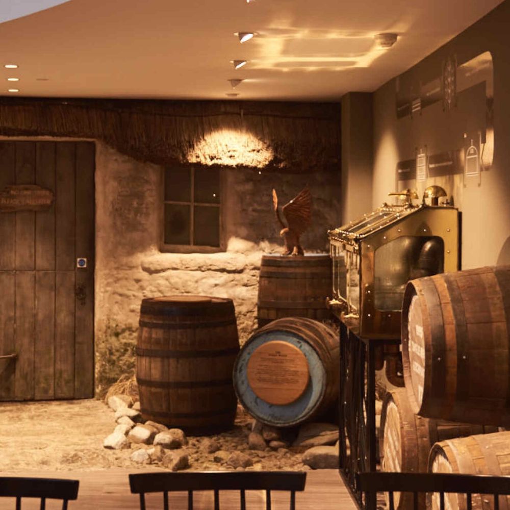 Distillerie de whisky écossais Arran : Salle de vieillissement avec tonneaux de whisky, décor rustique en pierre et machine à spirit safe, ambiance chaleureuse typique des distilleries.