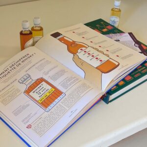 Miniature article de blog Livres sur le whisky Le club des connaisseurs : Livres de dégustation sur le whisky ouverts, expliquant comment lire une étiquette de bouteille, accompagnés de fioles de whisky pour une initiation à la dégustation.