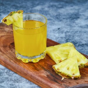 Verre de jus d’ananas frais avec morceaux d’ananas Victoria sur planche en bois – boisson exotique rafraîchissante et fruitée.